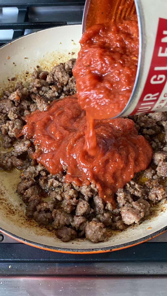 Add crushed tomatoes to the browned Italian sausage.