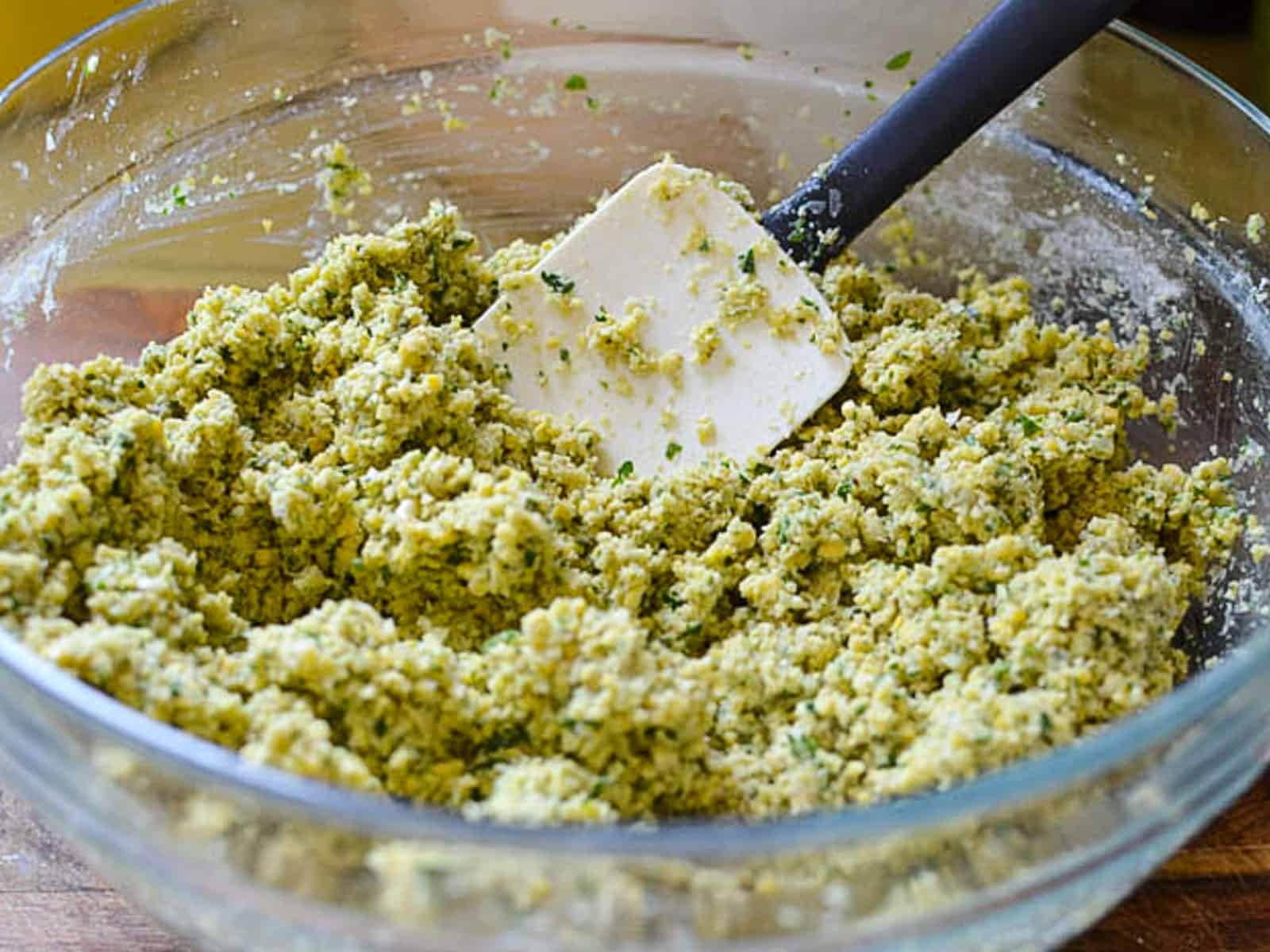 In the same food processor, add the herbs, garlic, onion and spices and pulse until there are no large pieces left. Add the herb mixture to the ground chickpeas along with the four, baking powder and baking soda and stir to combine.