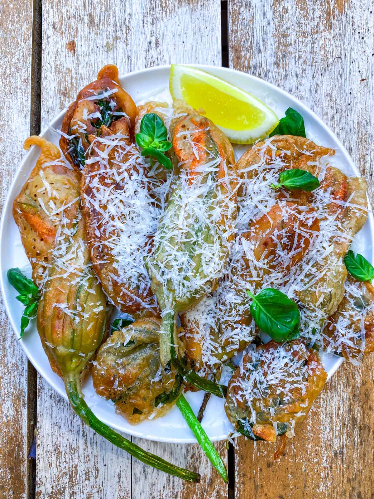 Squash flower fritters dusted with Parmesan and garnished with fresh basil and lemon.