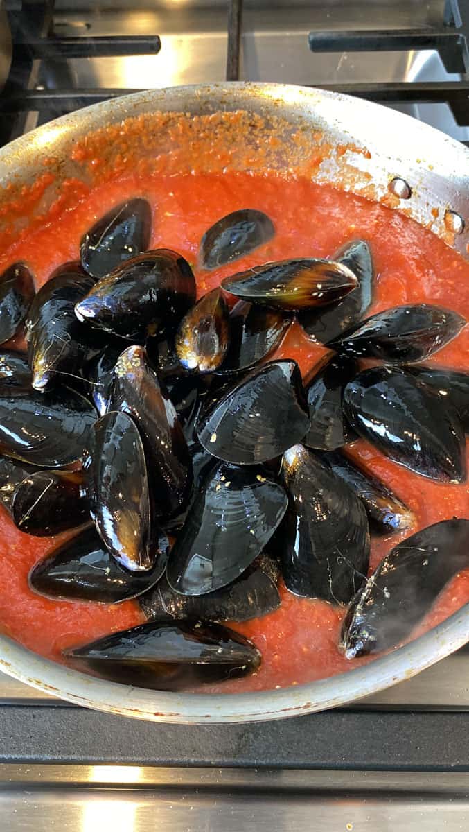 Add clean mussels to simmering marinara sauce and cook until the mussels just open.