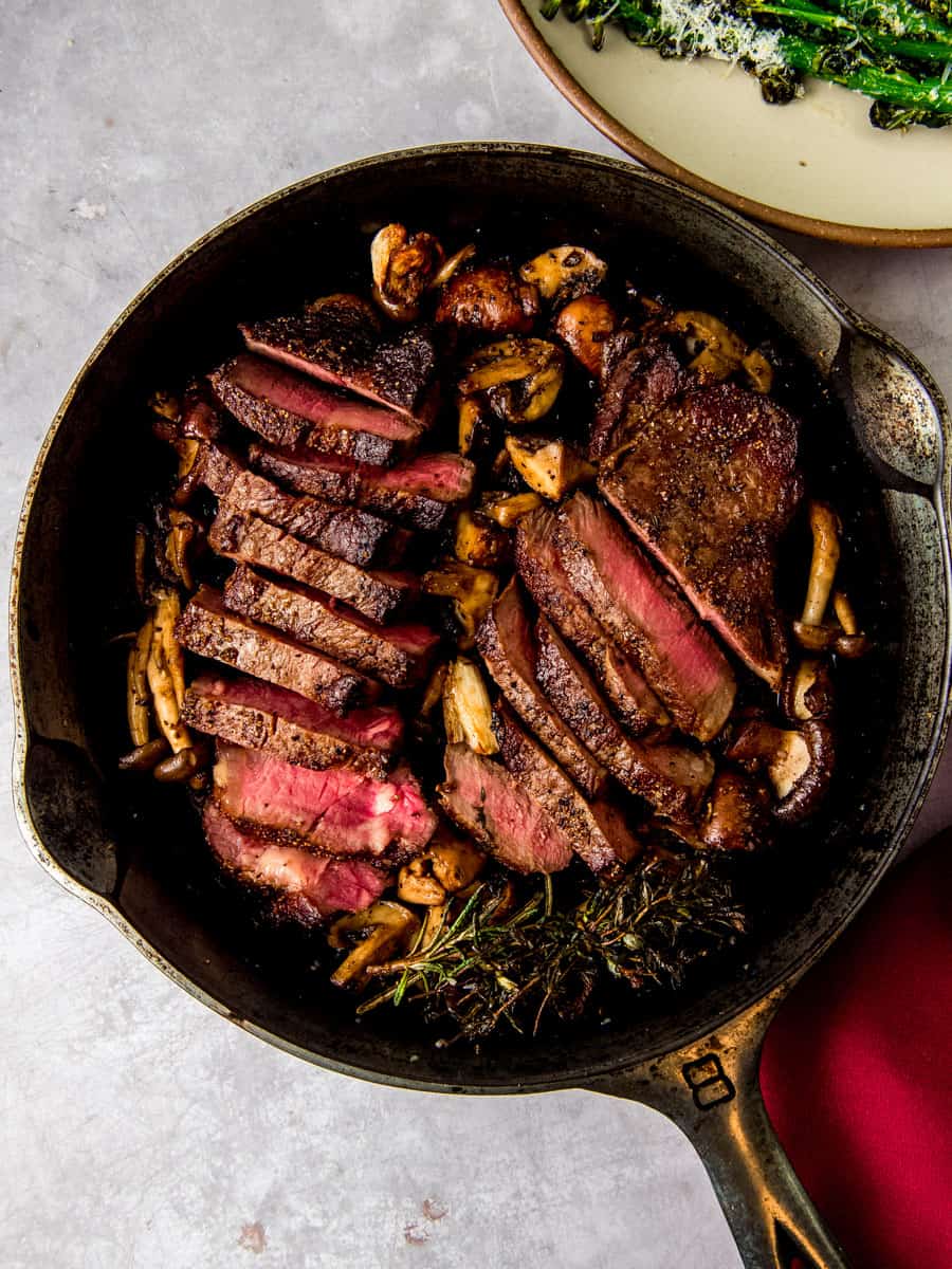 Seared cast iron New York strip steaks with mushrooms, garlic and herbs.