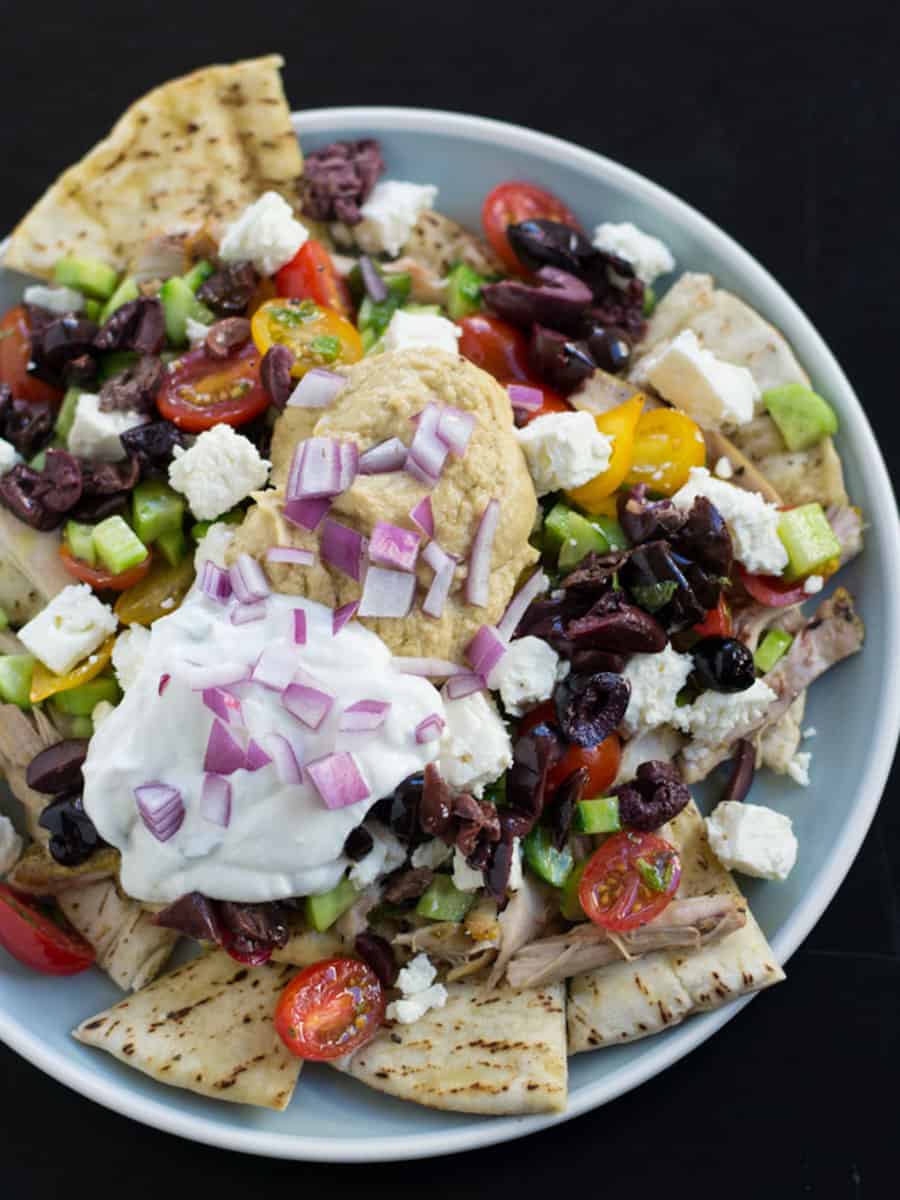 Greek nachos layered with yogurt, hummus and black olives.