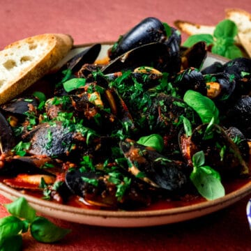 Steamed mussels in marinara sauce topped with fresh basil leaves.