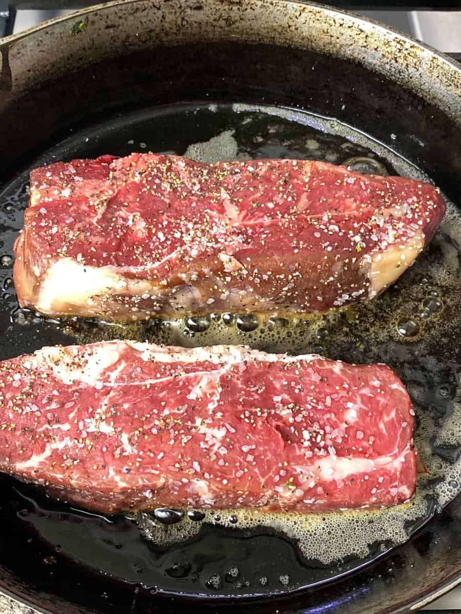 Sear the New York strips in a hot cast iron skillet with butter.