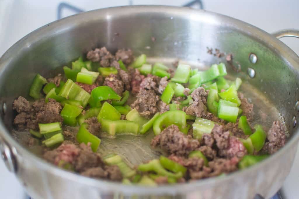 Add the chopped green peppers to the meat mixture and cook until the peppers are just tender.