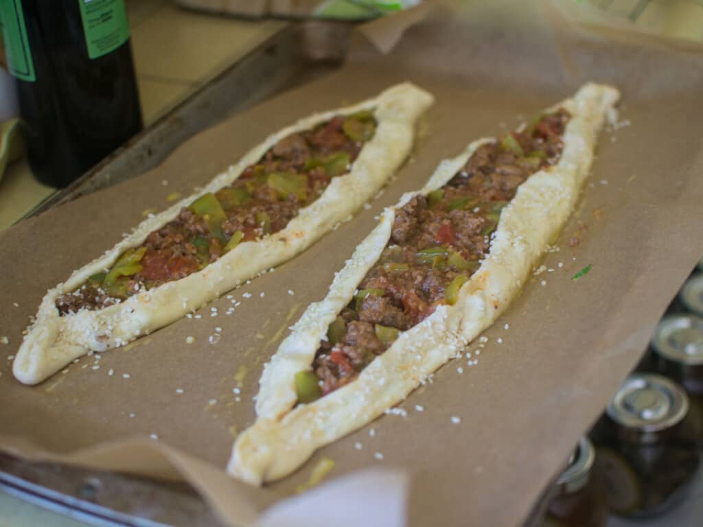Place the meat pide on a baking sheet and garnish with sesame seeds before baking.