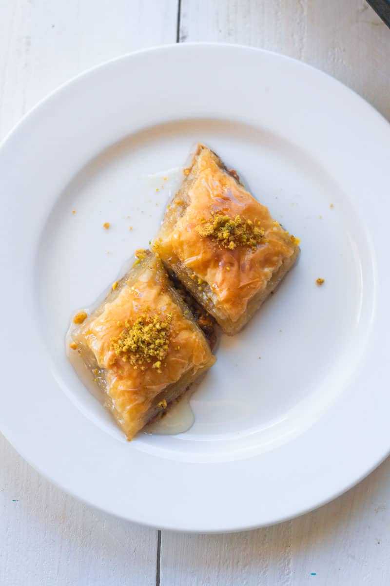 Two squares of pistachio baklava are garnished with crushed pistachios on top.