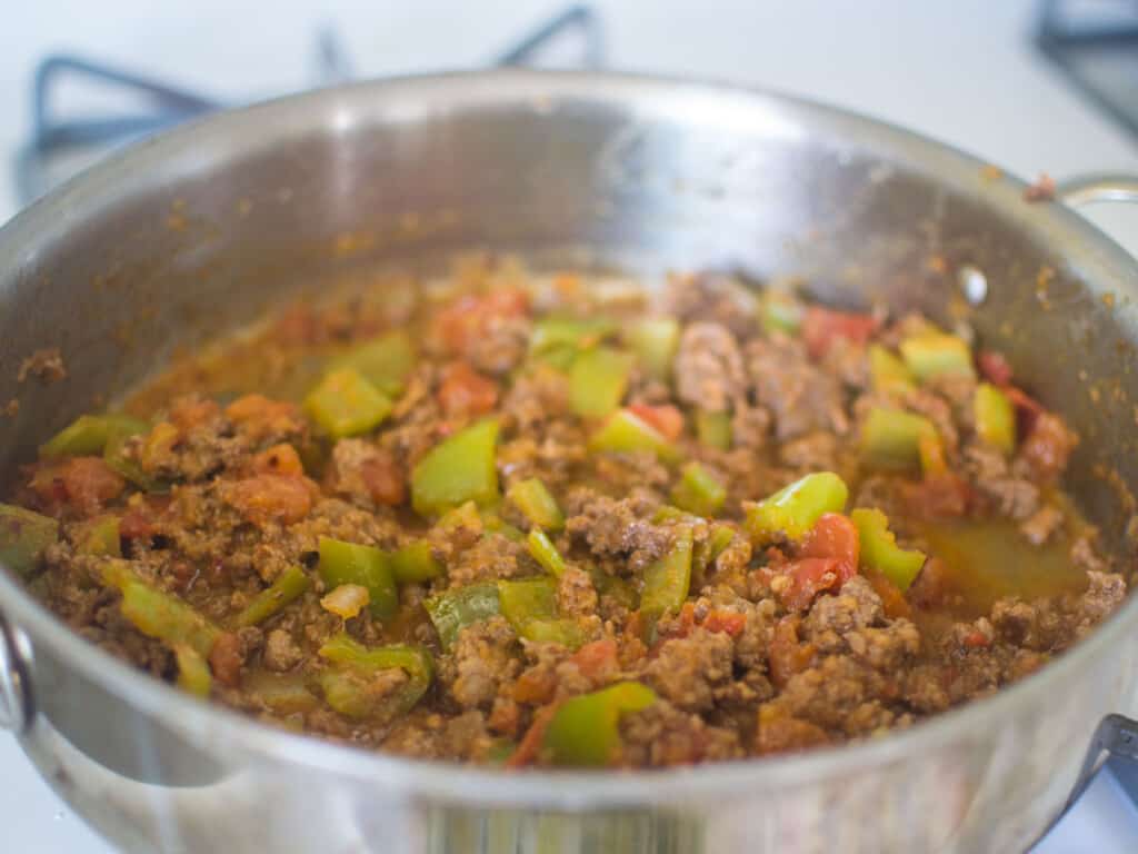 Add the tomatoes and peppers to the spiced ground meat mixture and cook until the vegetables are softened.