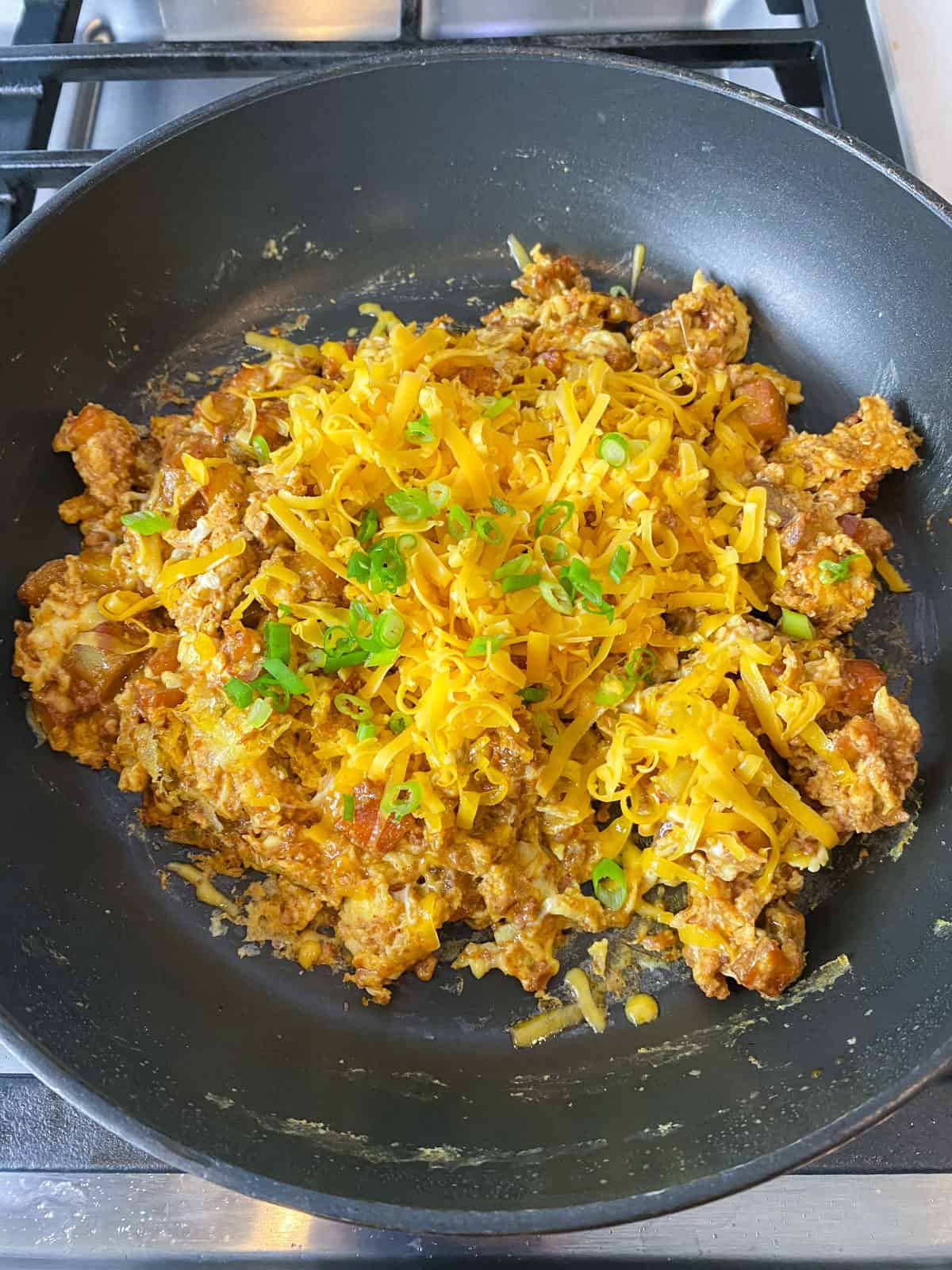 Add shredded cheddar cheese and green onions to the chorizo and egg scramble.