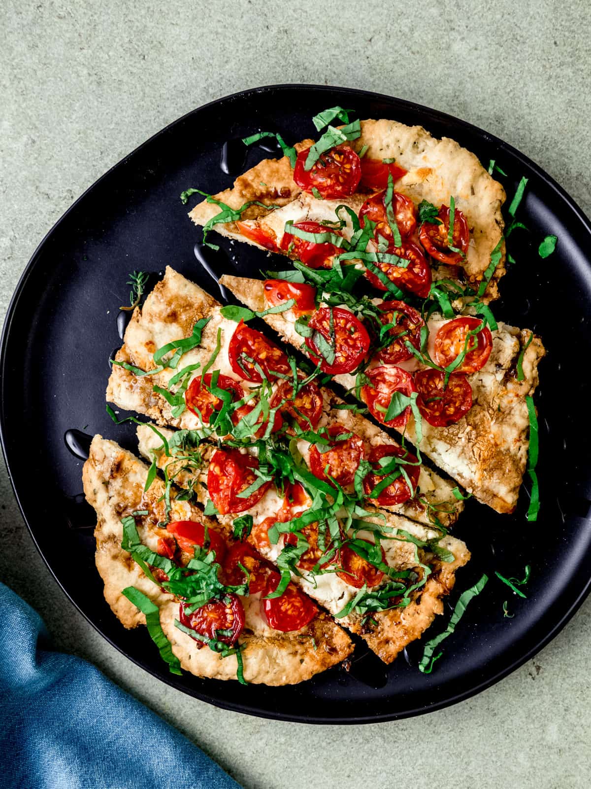 Bake the cheese and tomato flatbread until crisp and garnish with balsamic glaze and fresh herbs.