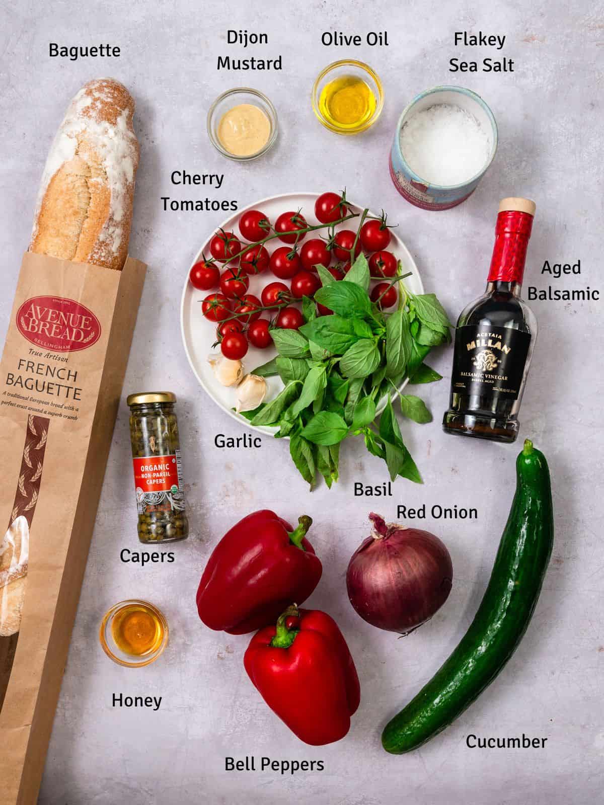 Ingredients for grilled panzanella salad including a baguette, cherry tomatoes, peppers and onions.