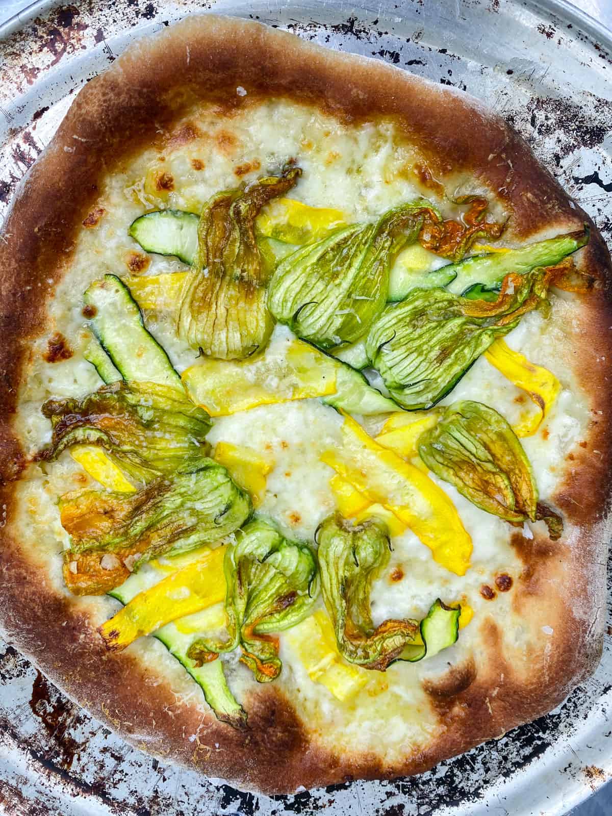 Cook the squash blossom pizza until cheese has melted and crust is golden brown.