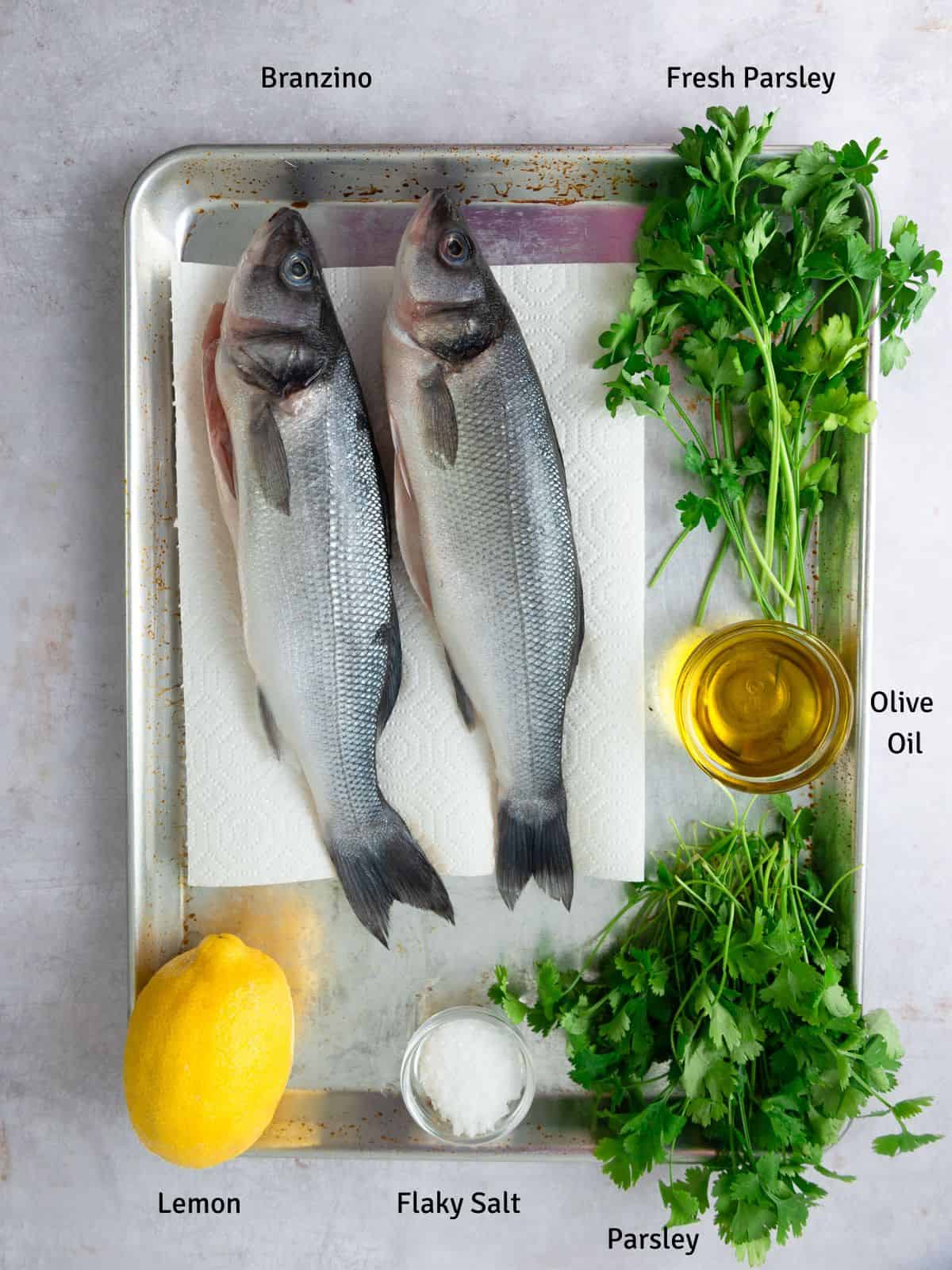Ingredients for grilled branzino, including lemon, olive oil and fresh herbs.