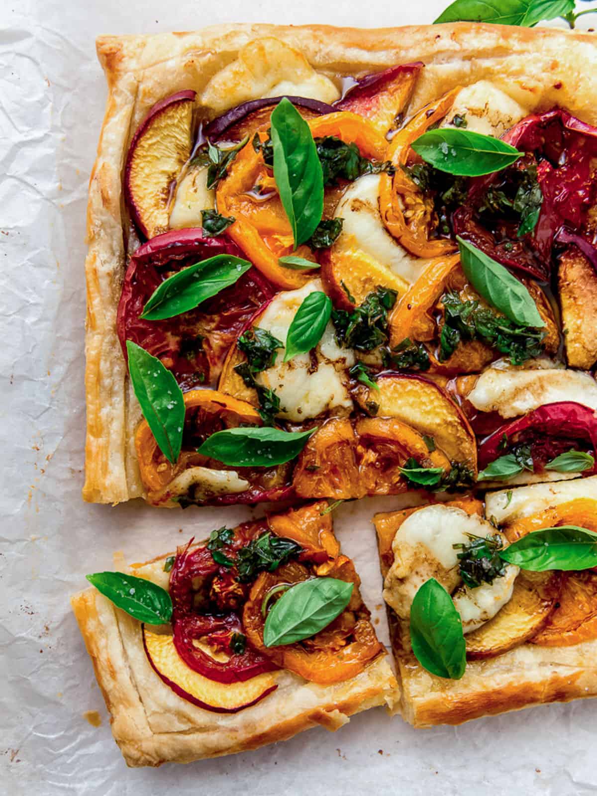 Peach caprese tart with puff pastry and garnished with basil oil and fresh basil leaves.