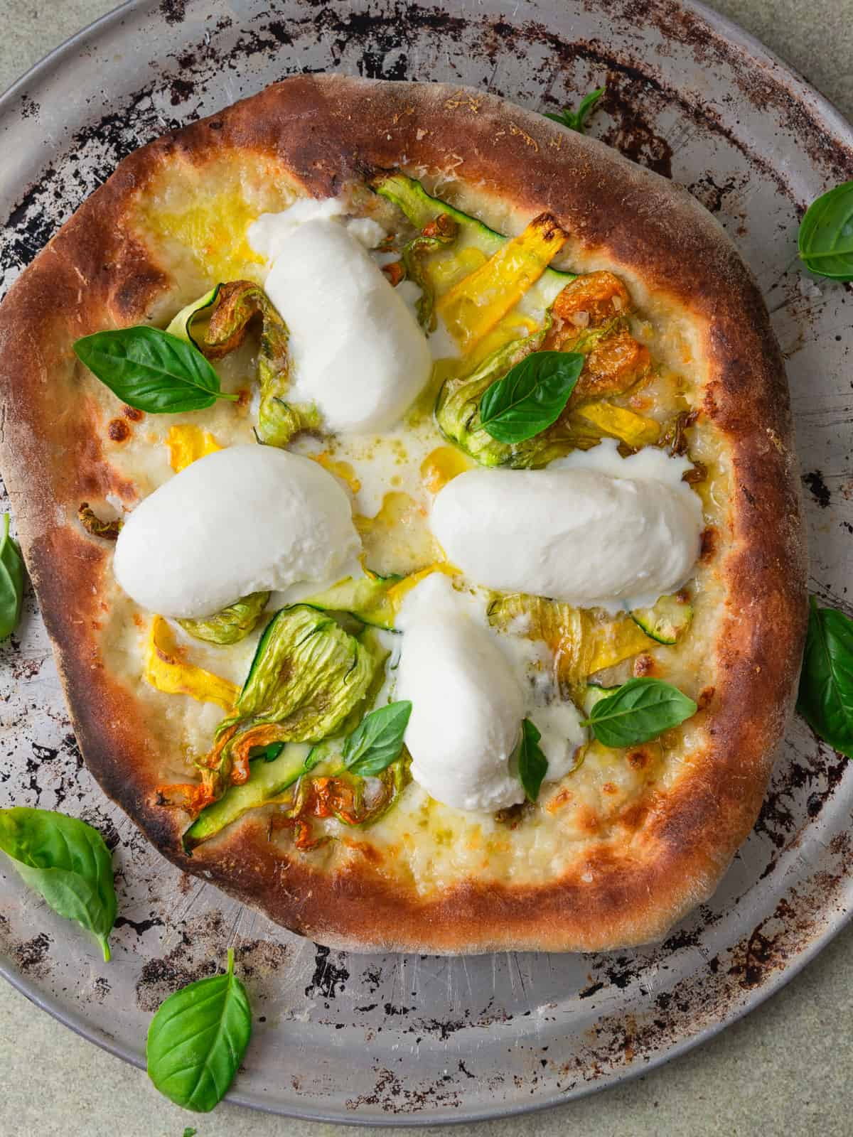 Zucchini flower and burrata pizza with thinly sliced zucchini and fresh basil.