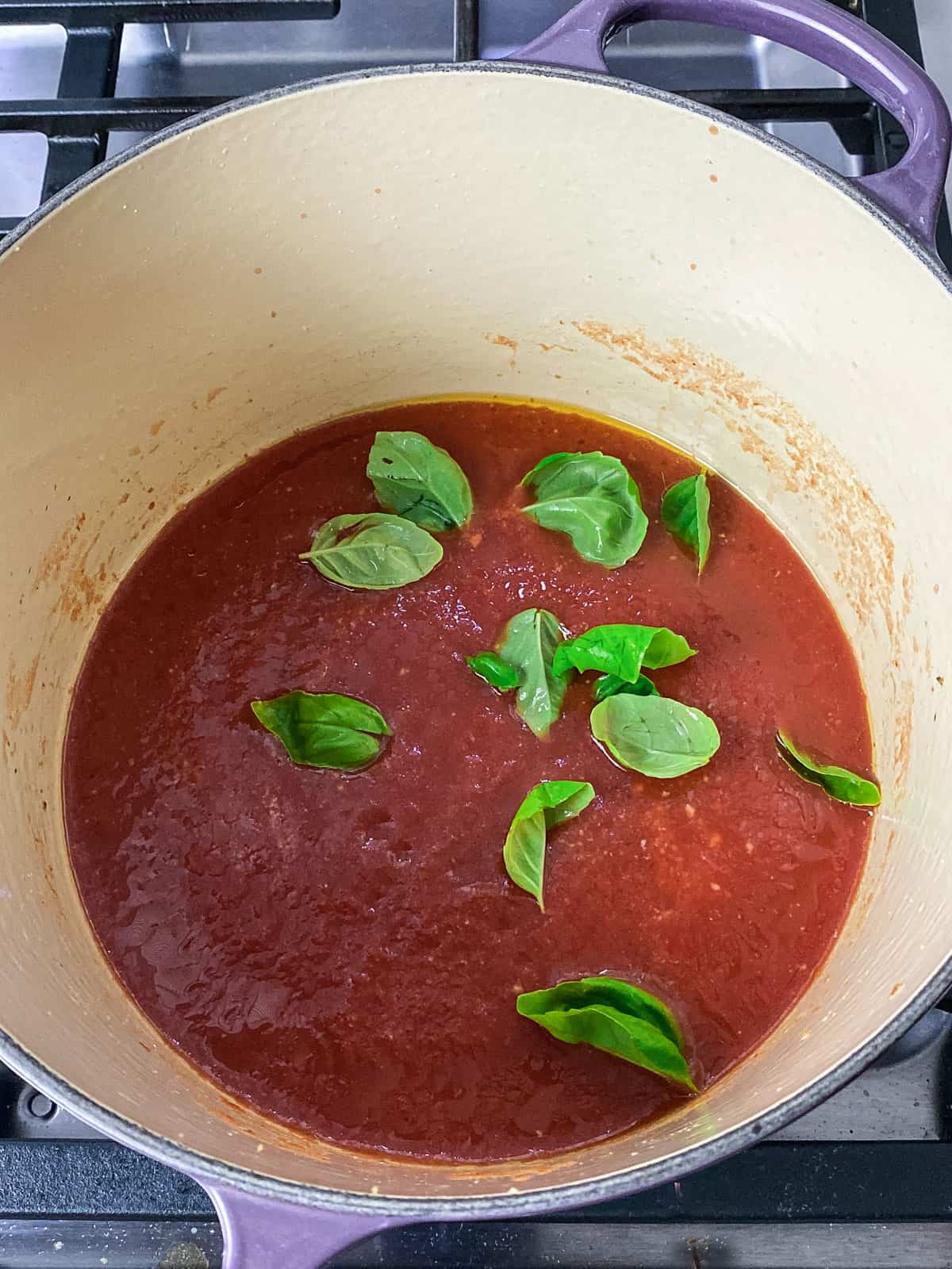 Add fresh basil leaves to the tomato sauce.