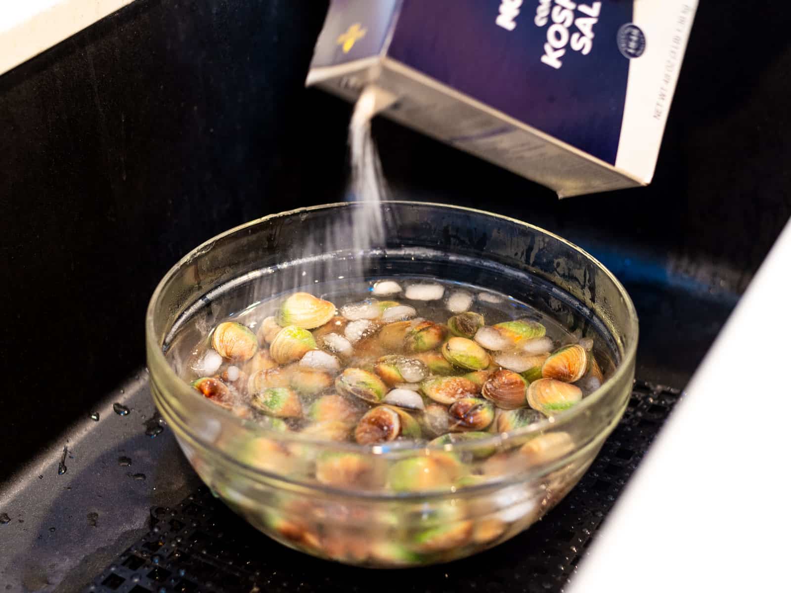 Place the clams in a large bowl filled with ice cold water and sprinkle salt into the water, which will help the clams purge any sand out.