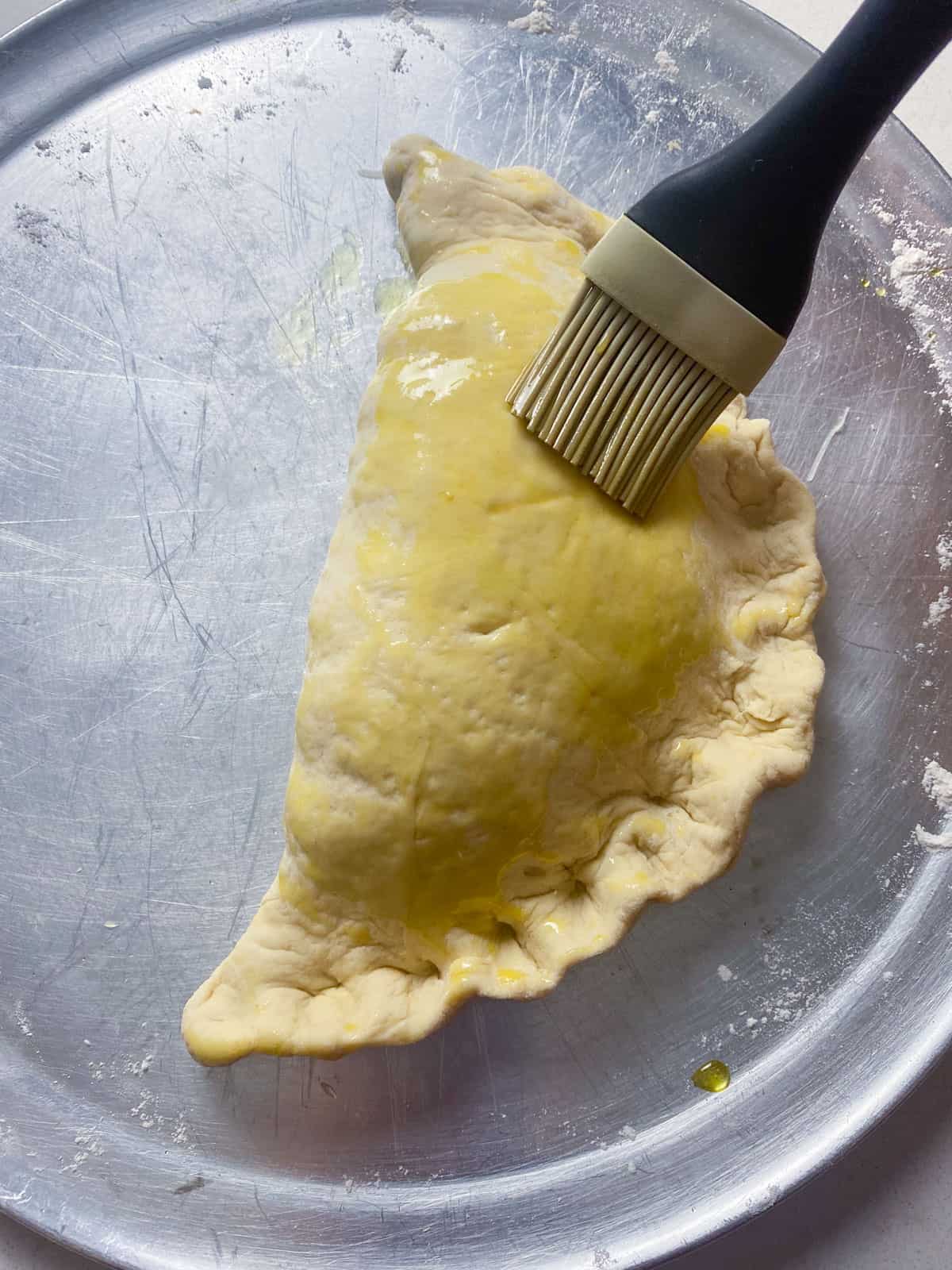 Brush olive oil onto the folded calzone before baking in the oven.