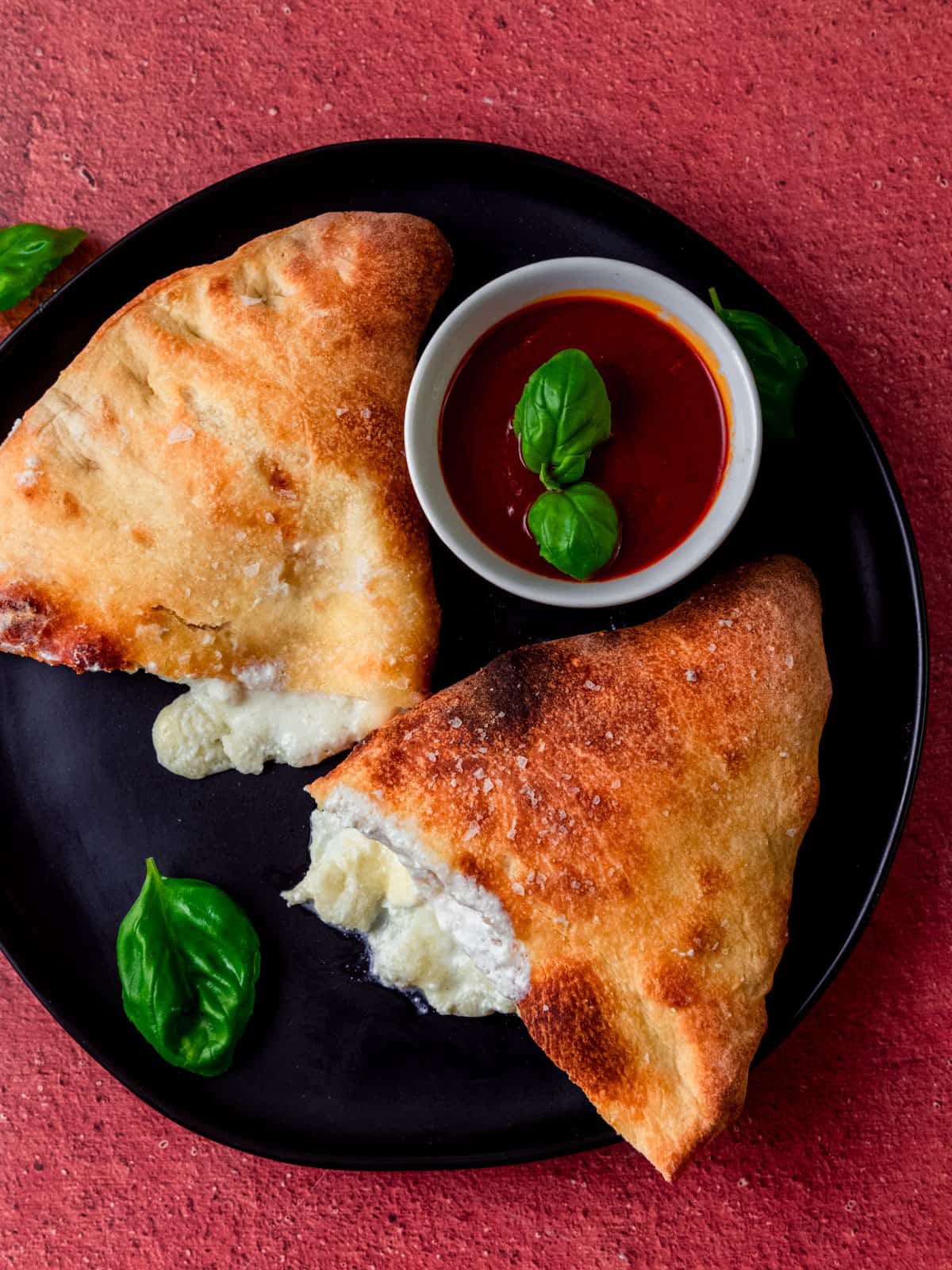 Four cheese calzone with a perfectly golden crust that is served alongside simple marinara sauce for dipping.