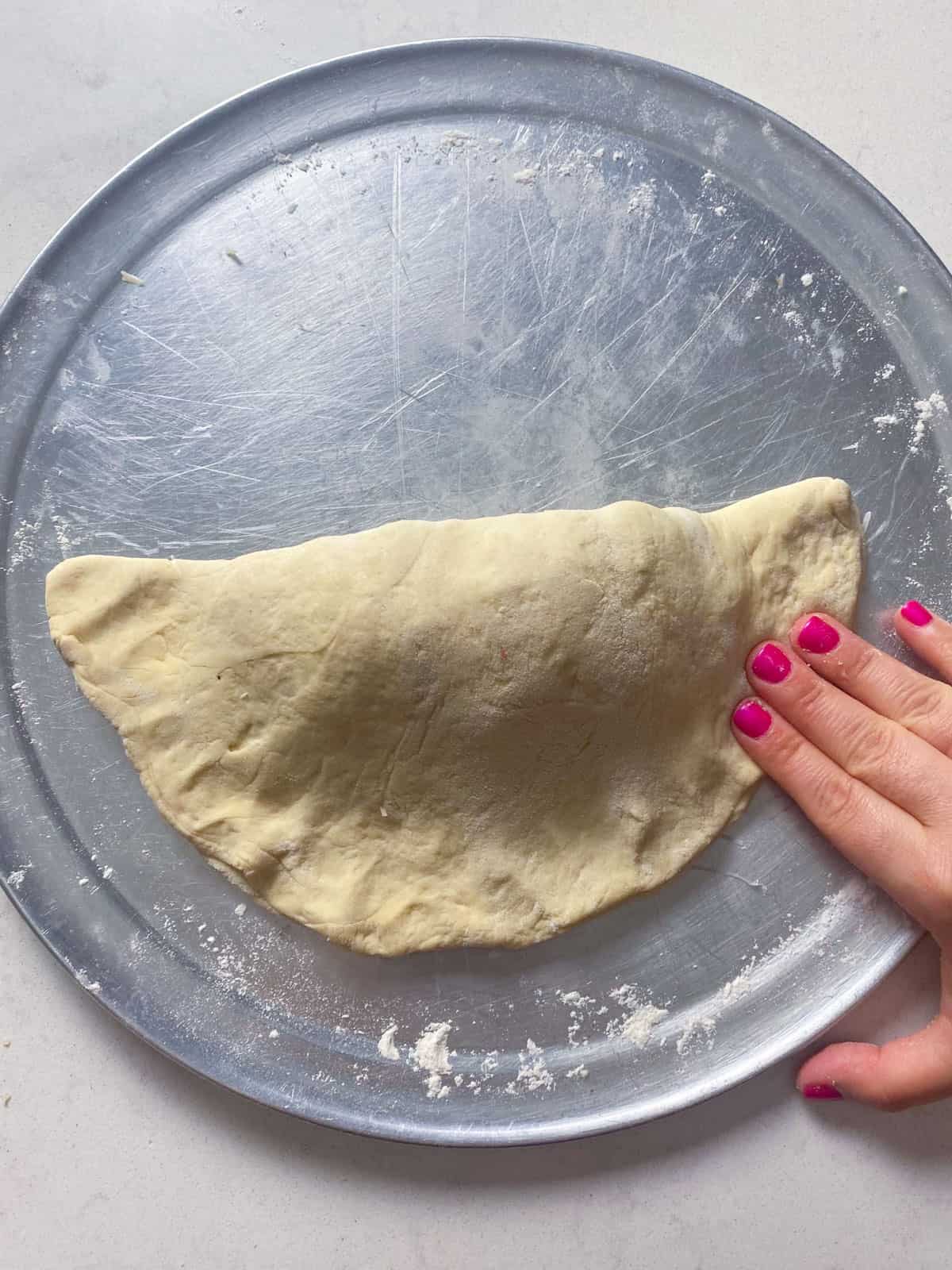Fold the calzone and crimp the pizza dough around the edges so the cheese is sealed inside.