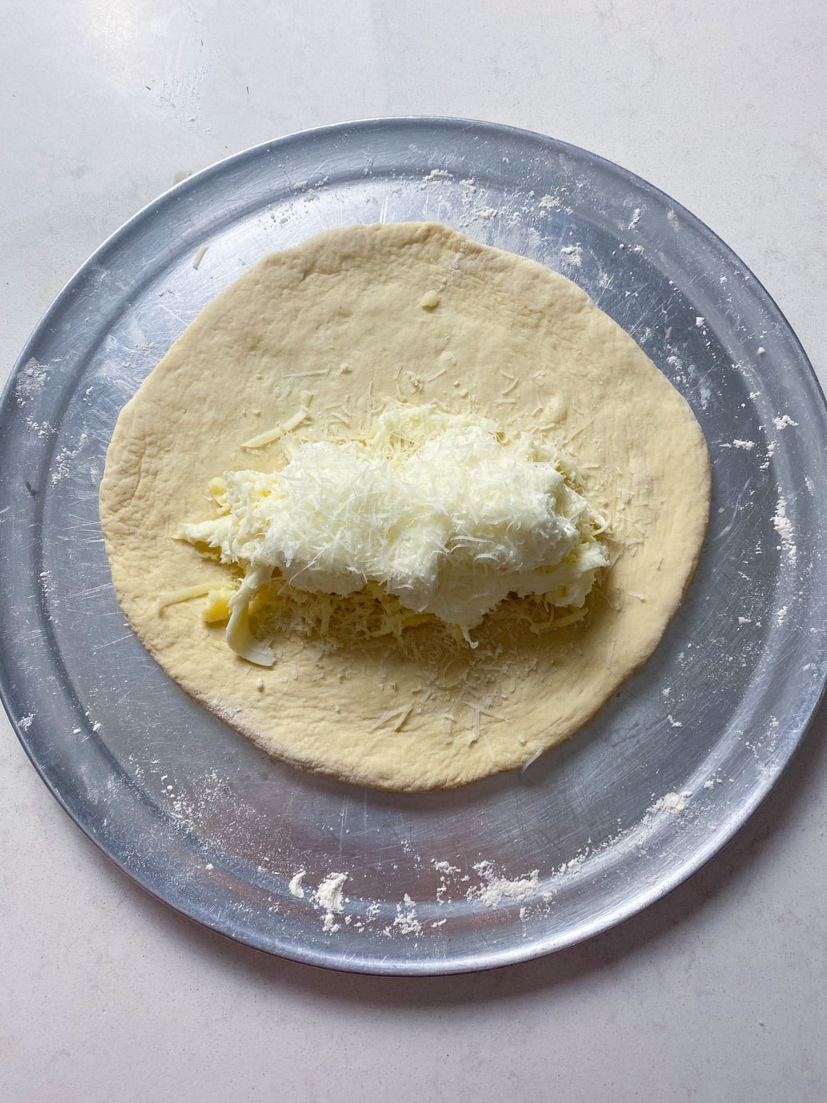 Once the pizza dough is stretched out, layer the four cheeses towards the lower center of the dough.