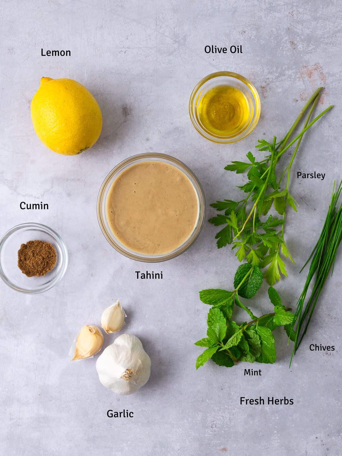 Ingredients for lemon tahini sauce, including olive oil, garlic, cumin and fresh mint, parsley and chives.