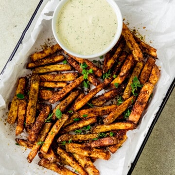 Baked zaatar fries are garnished with fresh thyme and served with a creamy herb tahini sauce.