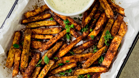 Baked zaatar fries are garnished with fresh thyme and served with a creamy herb tahini sauce.