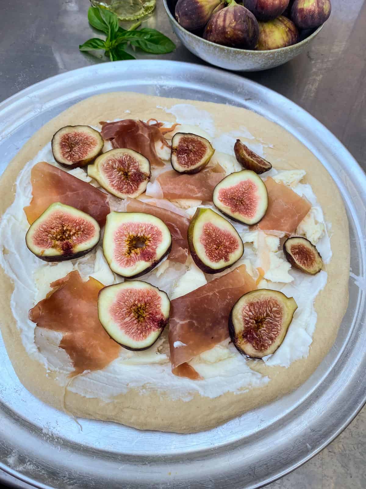 Once the cheese is on, layer slices of prosciutto and sliced fresh figs onto the pizza.