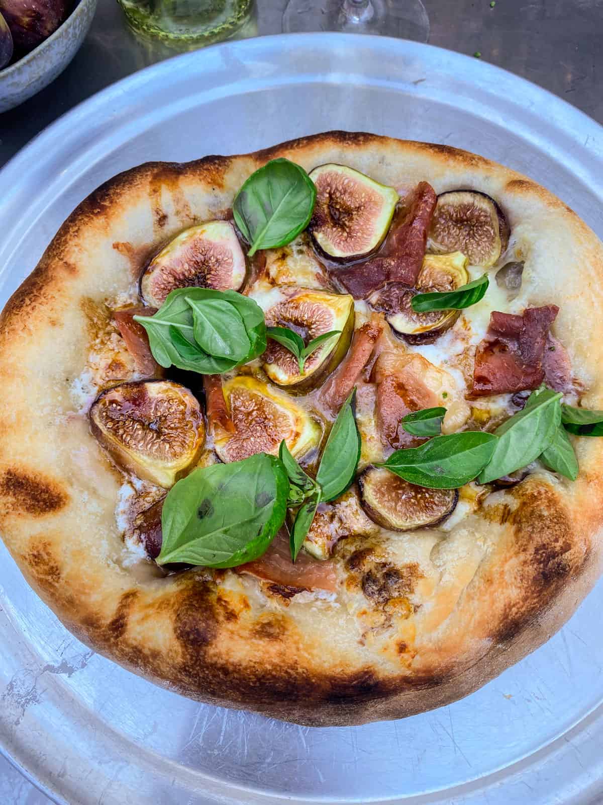 Once the prosciutto and fig pizza is golden brown and cooked through, garnish with drizzle of balsamic and fresh basil leaves,