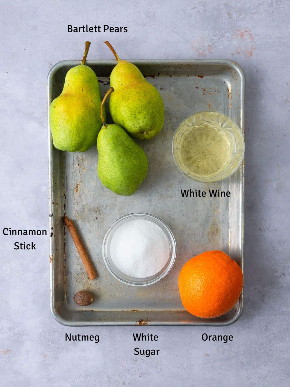 Ingredients for white wine poached pears, including cinnamon, nutmeg, orange and sugar.