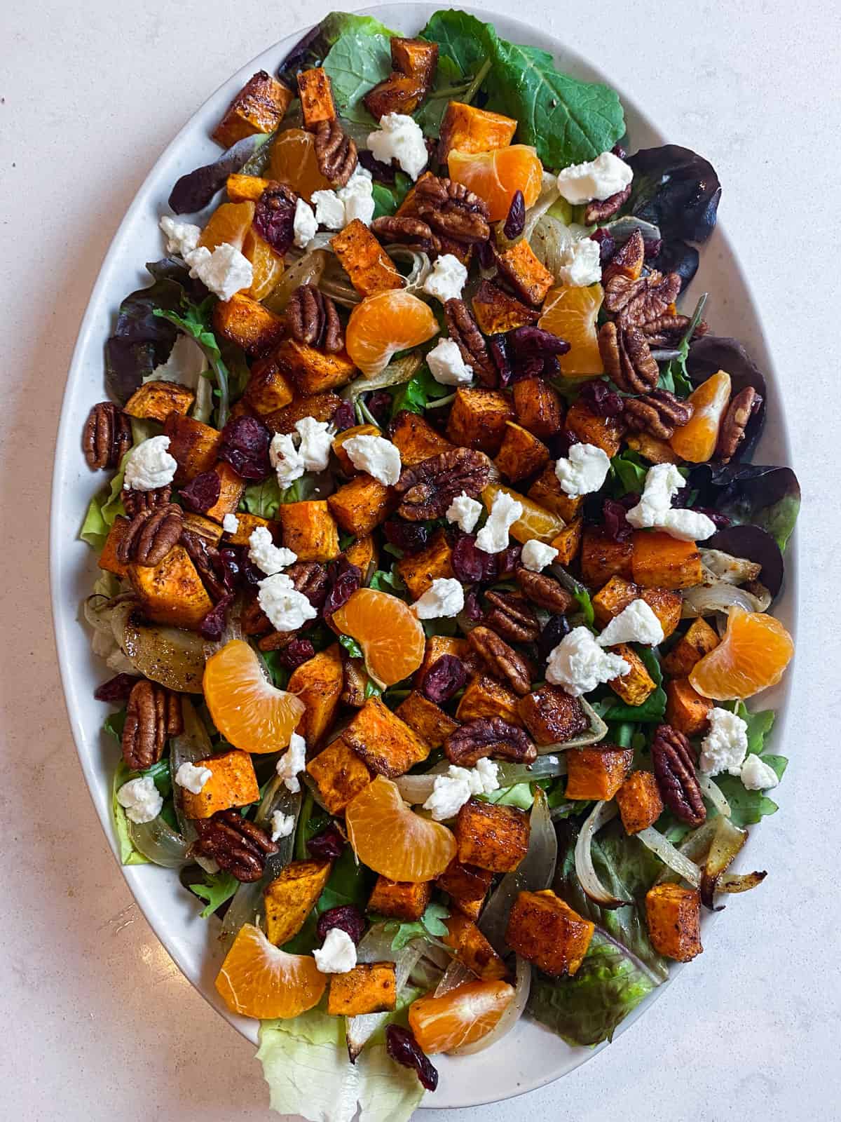 Layer clementine segments, candied pecans, dried cranberries and goat cheese onto the roasted sweet potato salad.