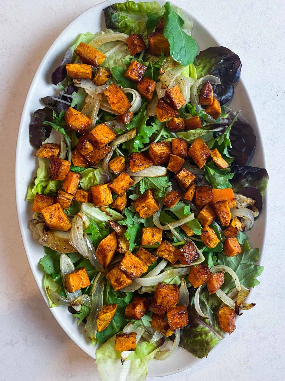 Layer the roasted sweet potatoes and caramelized onions on top of the salad greens.