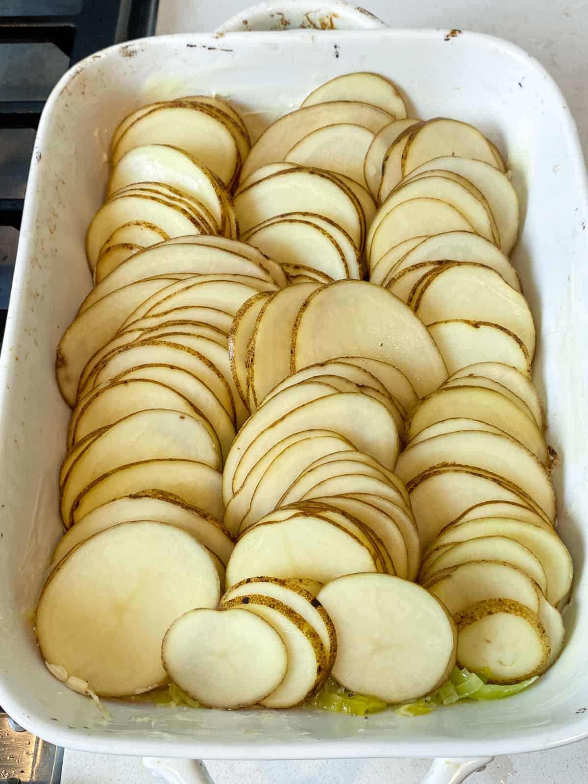 Layer the thinly sliced potatoes on top of the sautted leeks in the baking dish.