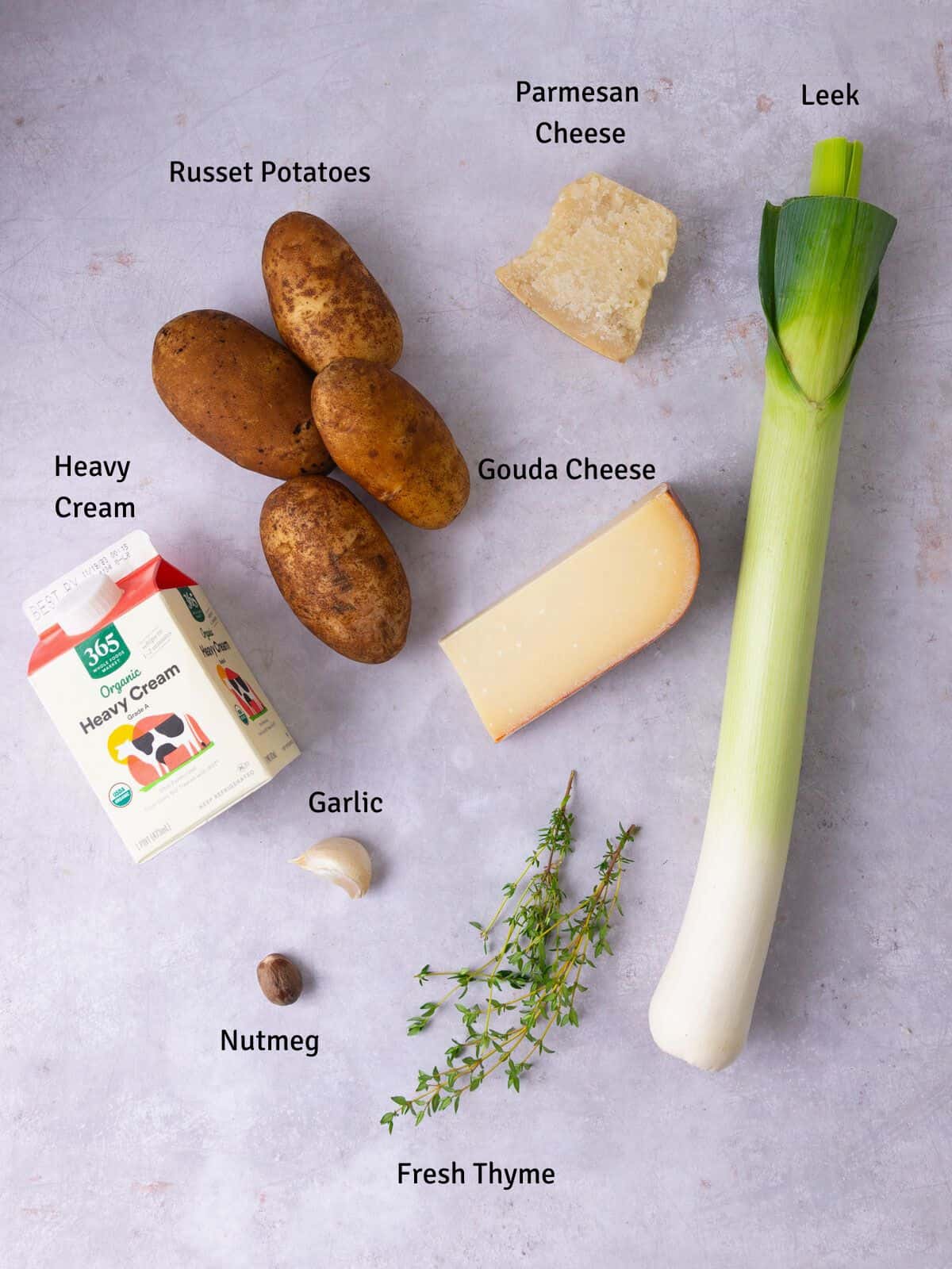 Ingredients for potato leek gratin including heavy cream, gouda cheese, nutmeg and fresh thyme.
