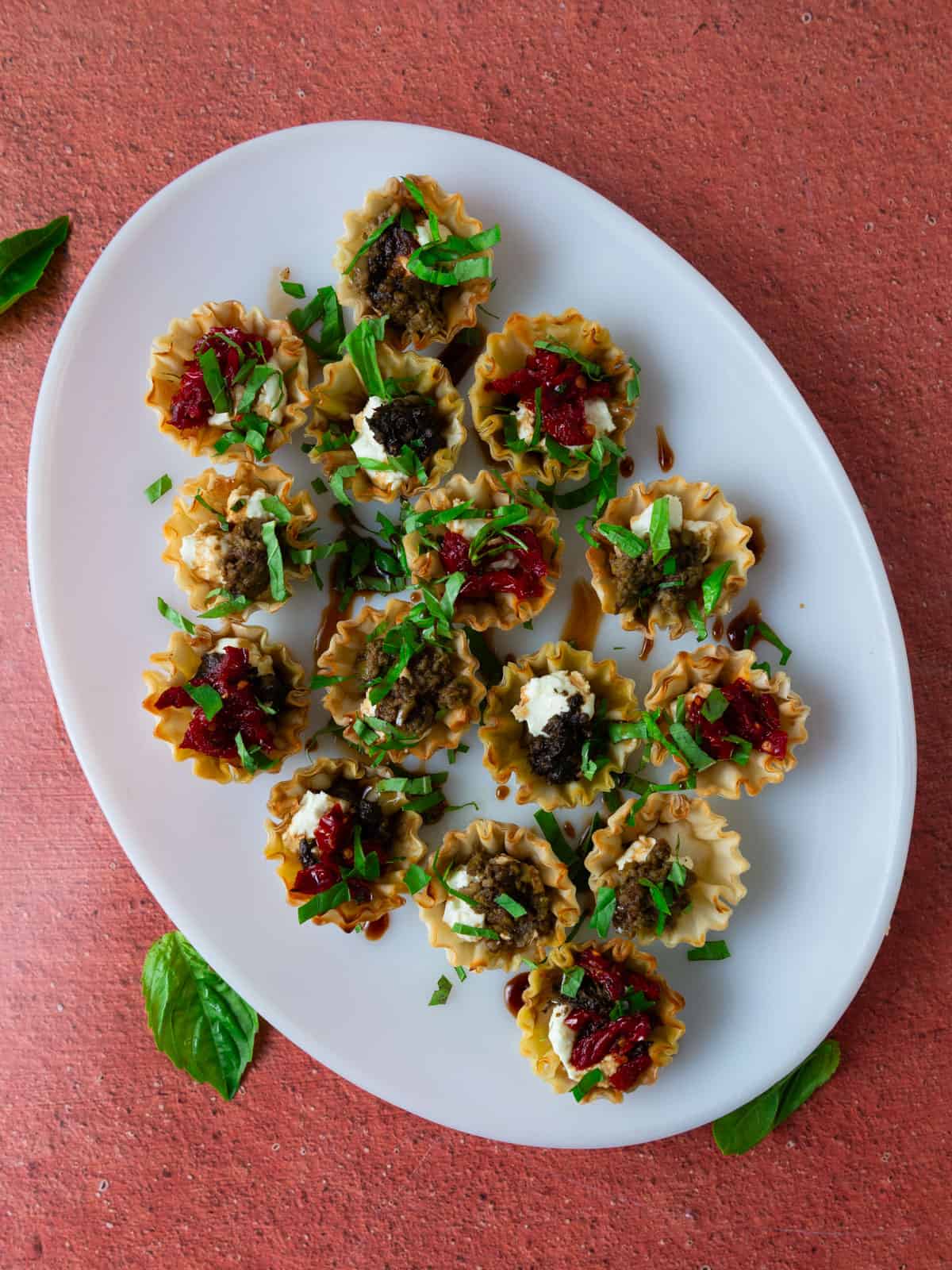 Goat cheese stuffed phyllo cups with pesto, tapenade and sun-dried tomatoes. Garnish with balsamic and basil.