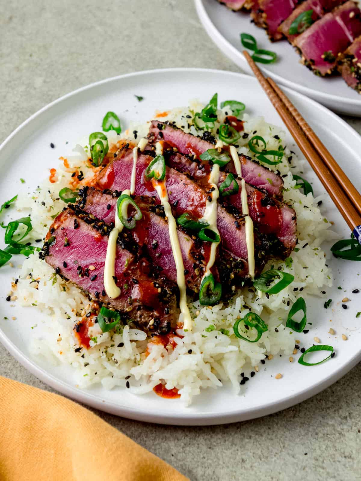 Seared ahi with furikake that is served over white rice and garnished with green onions and a drizzle of kewpie mayo and sriracha.