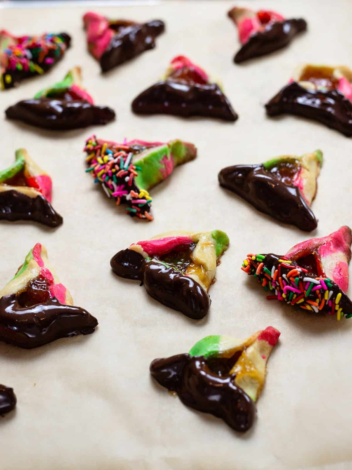 Baked rainbow hamantaschen cookies dipped in chocolate.