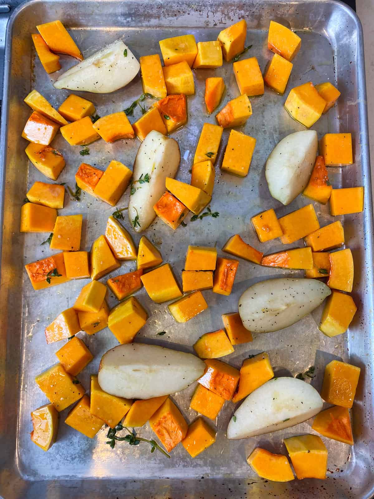 Add cubed butternut squash, pears and thyme onto a baking sheet and drizzle with olive oil.