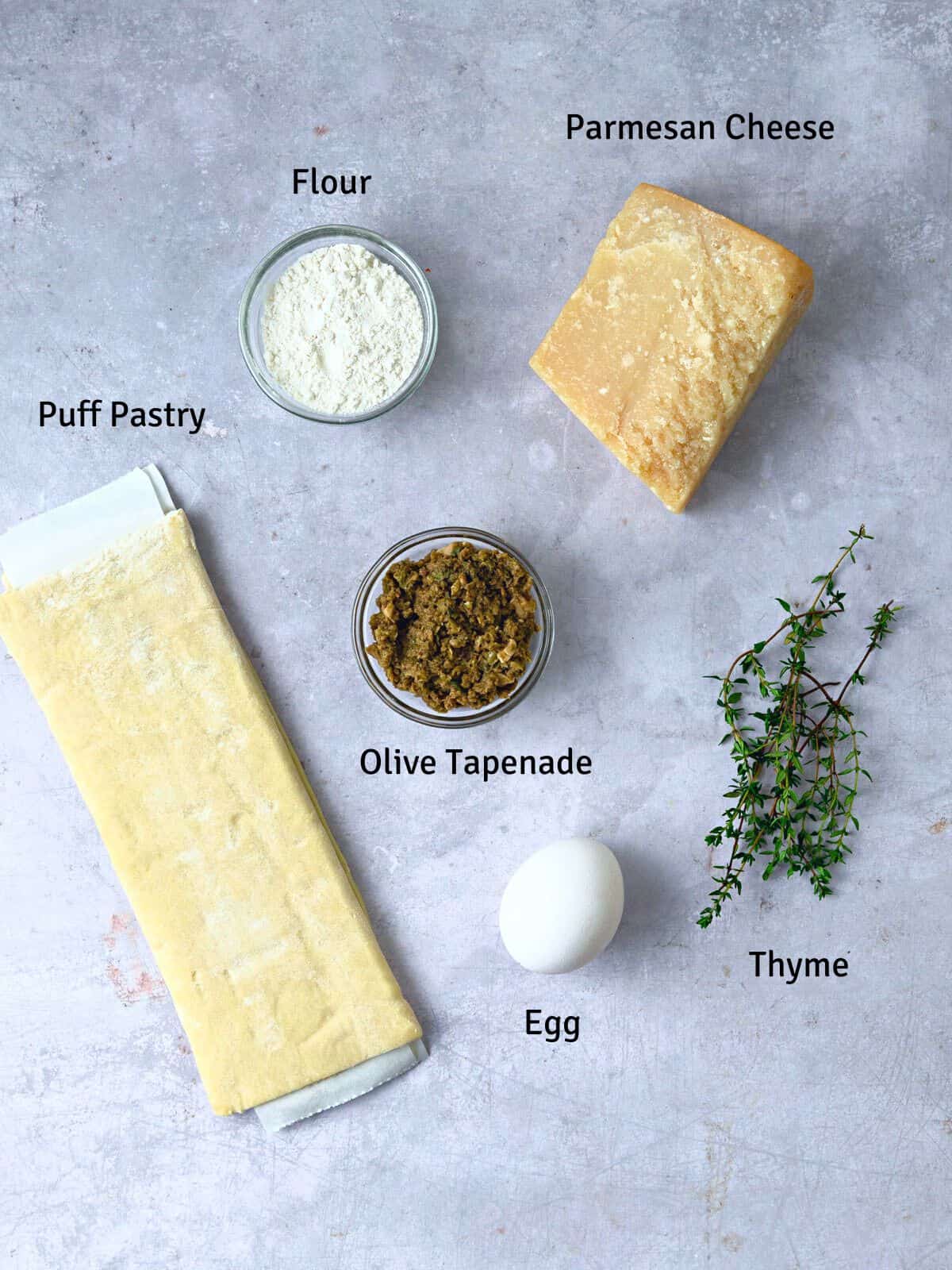 Ingredients for puff pastry straws, including Parmesan cheese, fresh thyme and olive tapenade.