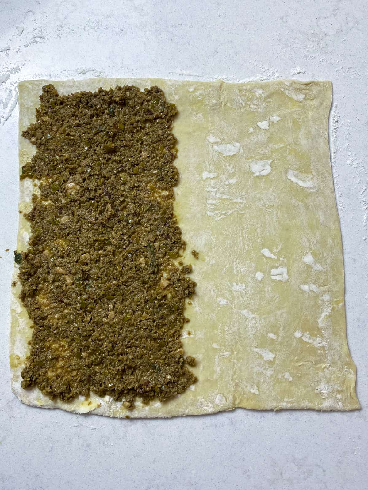 Spread a thin layer of olive tapenade onto half of the puff pastry sheet.