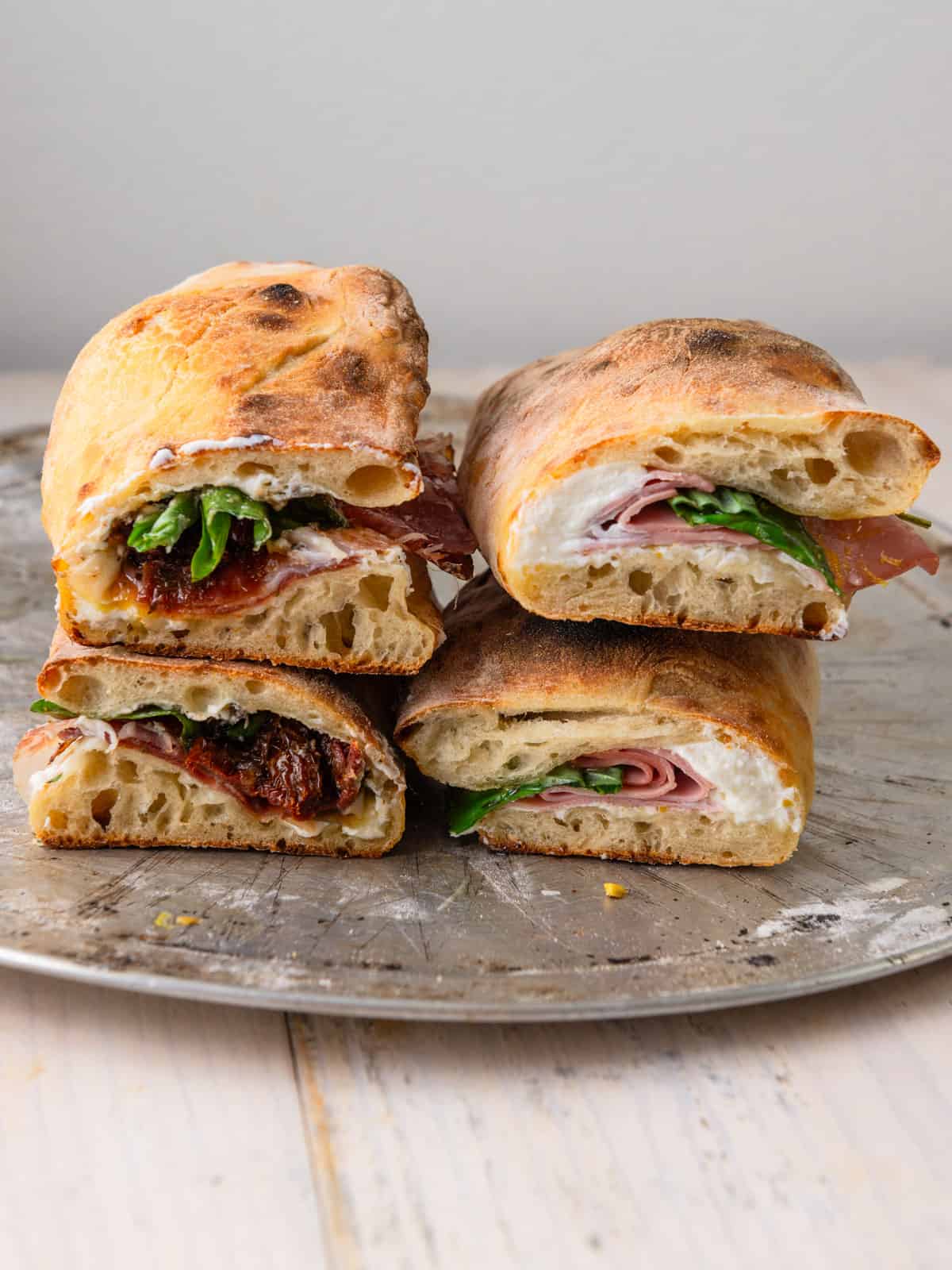 Two types of pizza sandwiches with cooked pizza dough that are filled with Italian meats, ricotta cheese and savory pesto.