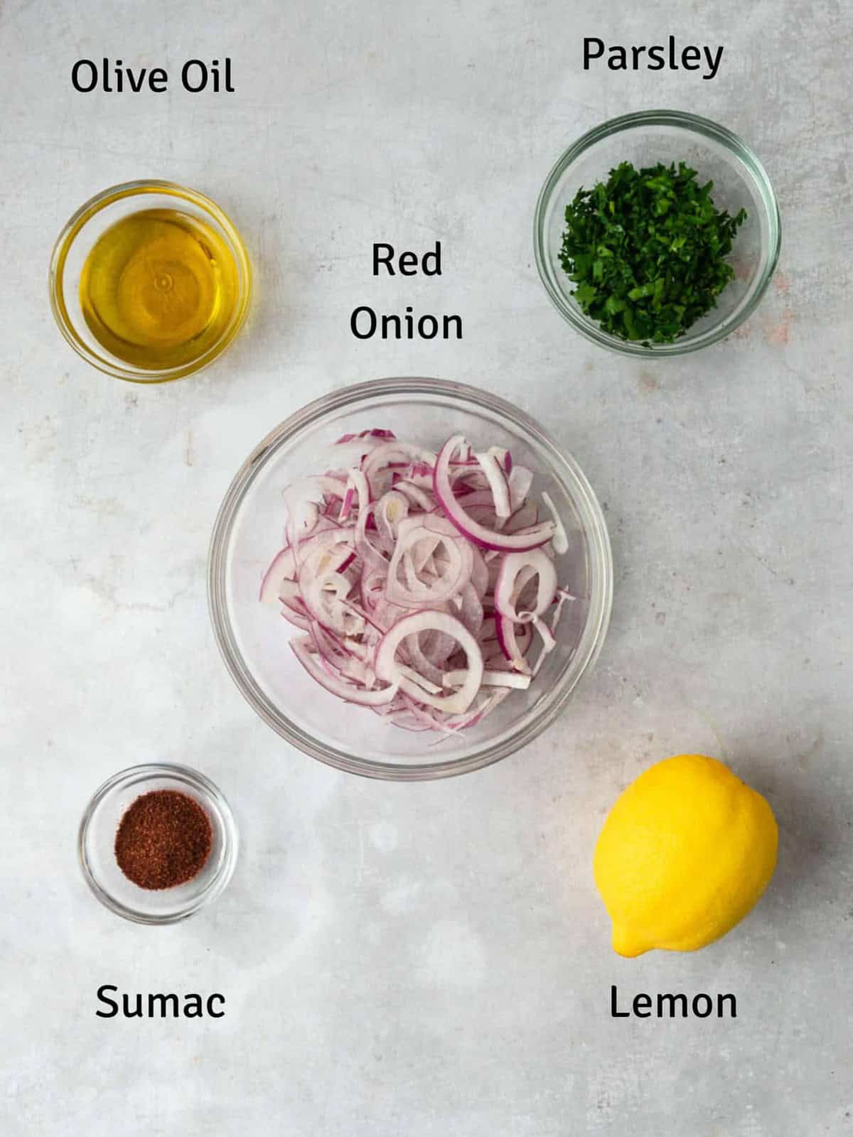 Ingredients for Turkish sumac onion salad including thinly sliced red onions, parsley, lemon and sumac.