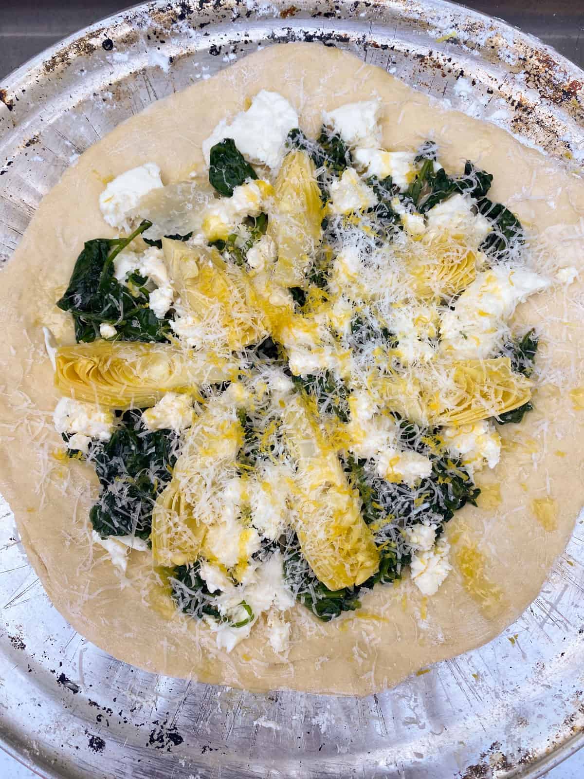 Layer the spinach, feta, mozzarella, artichoke hearts and grated parmesan onto the pizza dough.