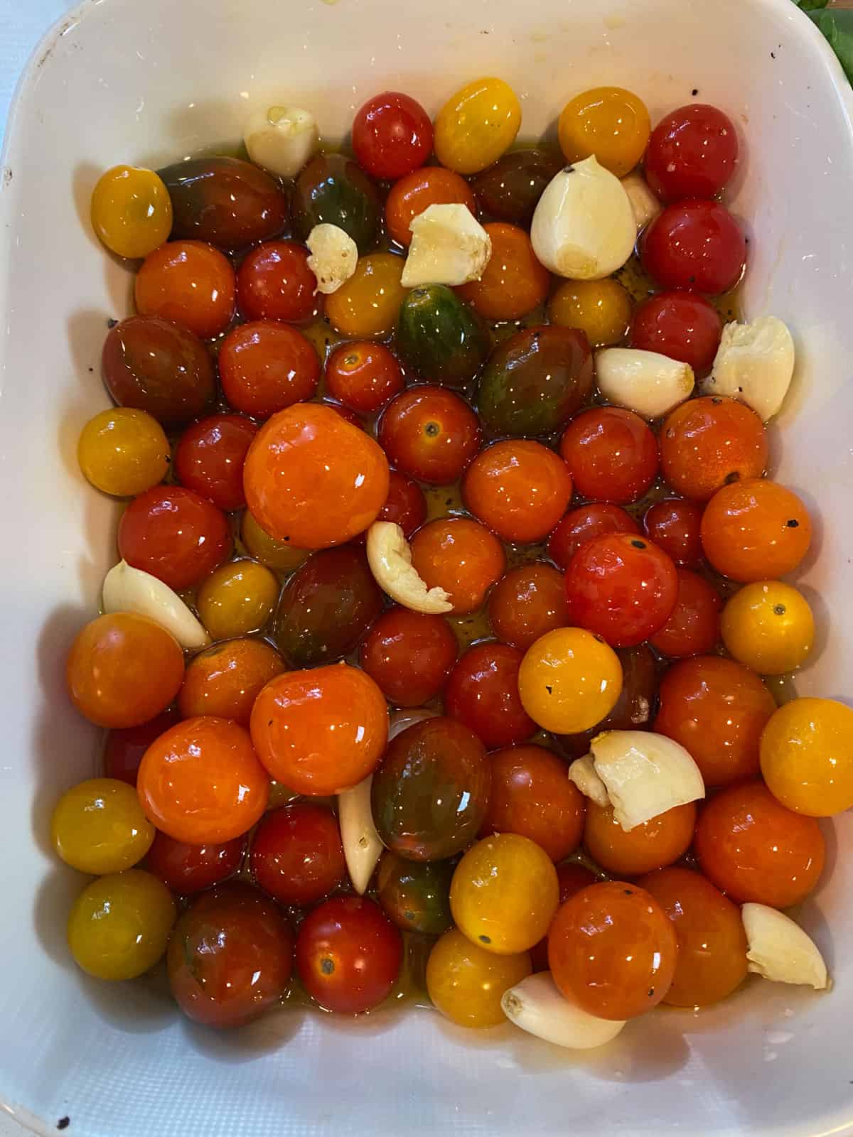 To a baking dish, add the cherry tomatoes, garlic cloves and season with salt, pepper and olive oil.