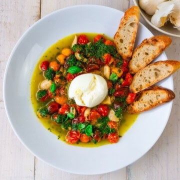 Tomato and garlic confit recipe served with creamy burrata cheese and crostini.