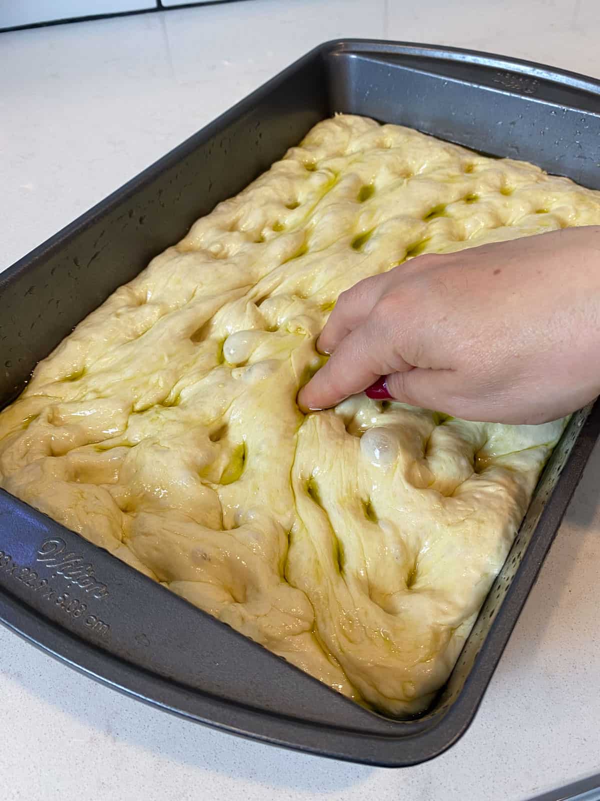 Use your fingers to press dimples into the focaccia dough.