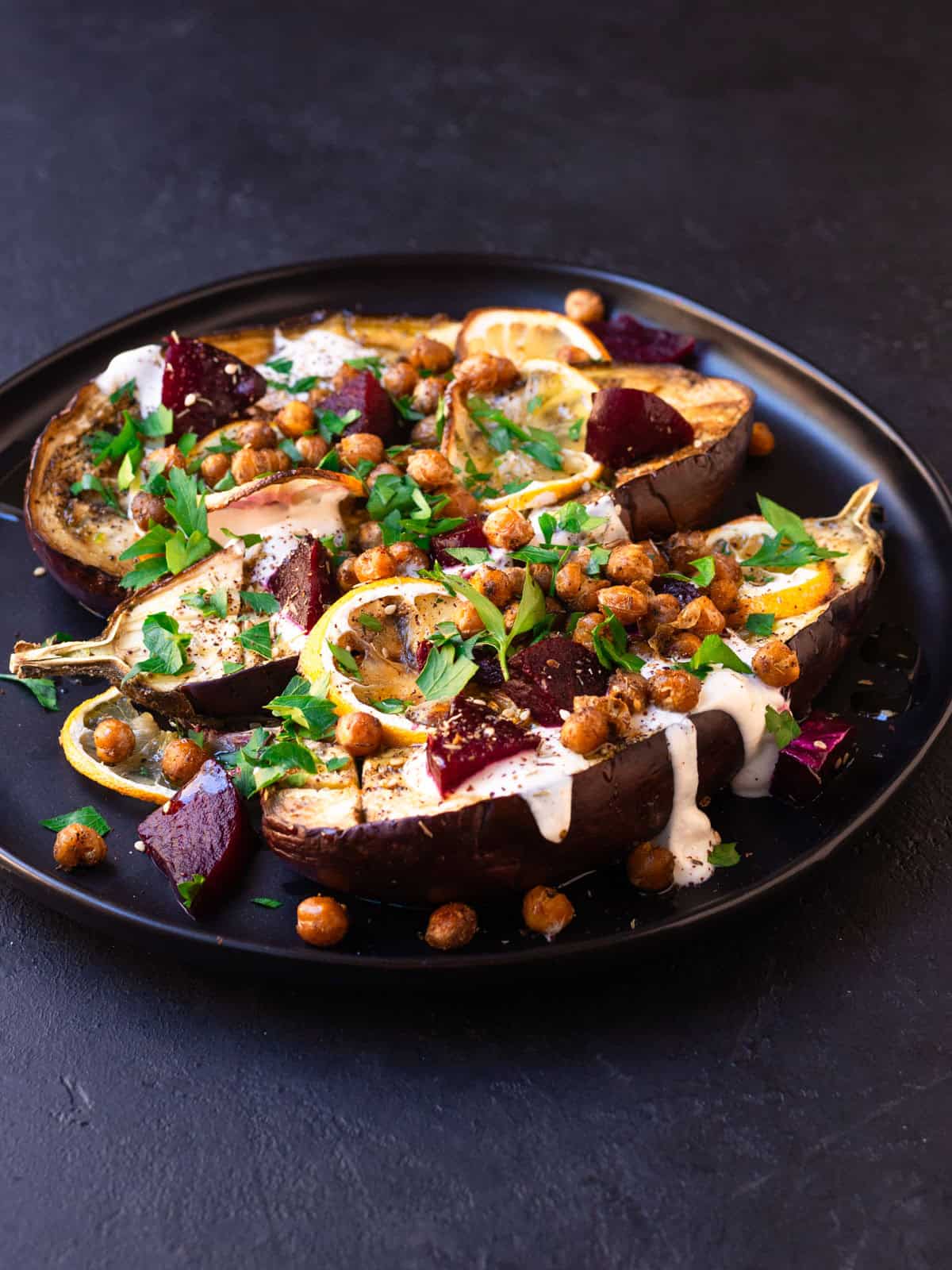 Mediterranean roasted eggplant is seasoned with warm spices and garnished with tahink, chickpeas and lemon.