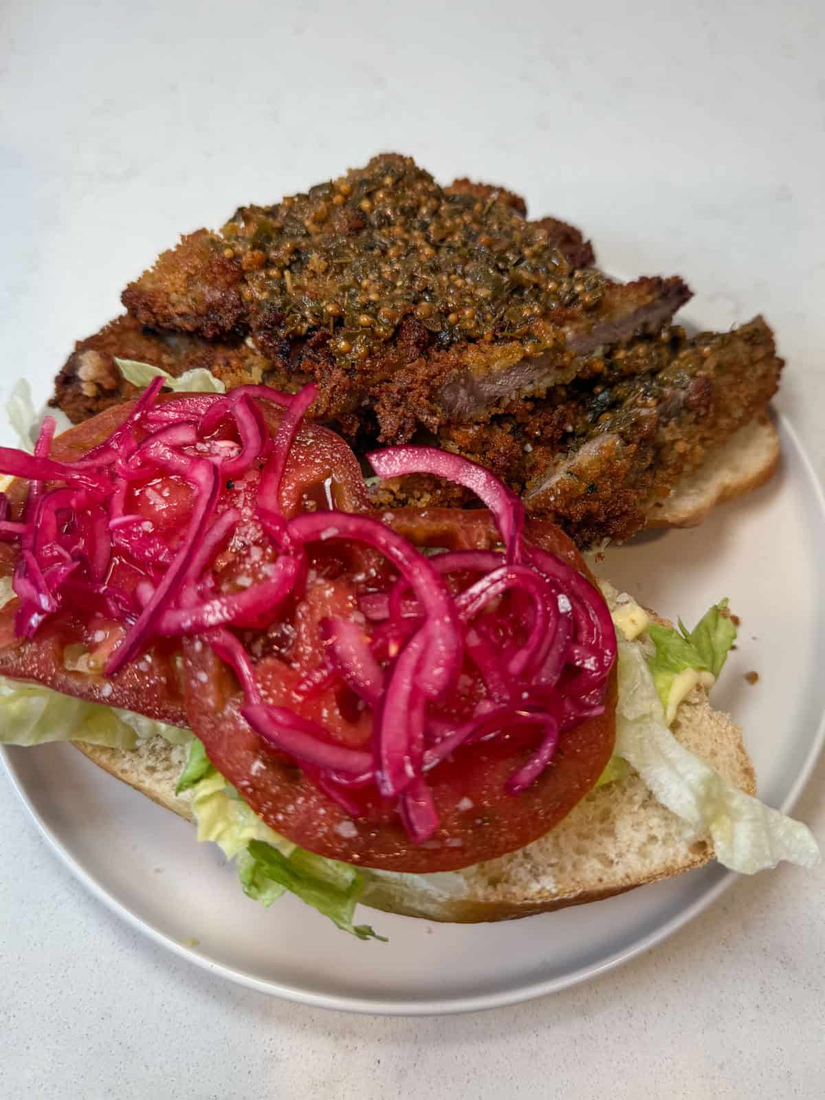 Layer the beef milanesa sandwich with lettuce, tomatoes, pickled onions and chimichurri.