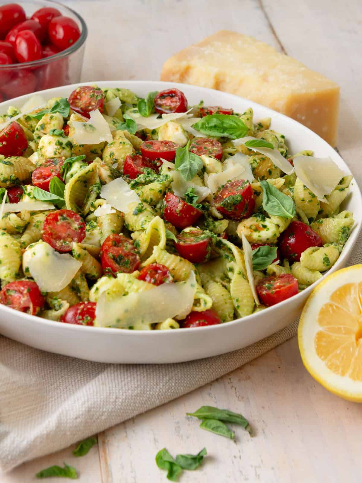 This caprese pasta salad is tossed with fresh basil pesto and finished with fresh basil and shaved Parmesan cheese.
